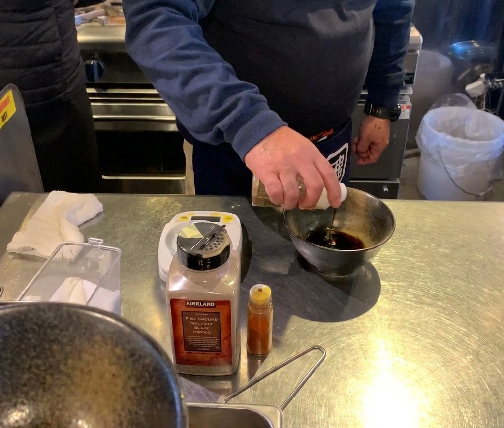 Une main versant du liquide dune bouteille dans un bol contenant déjà un petit monticule de fine poudre brune.
