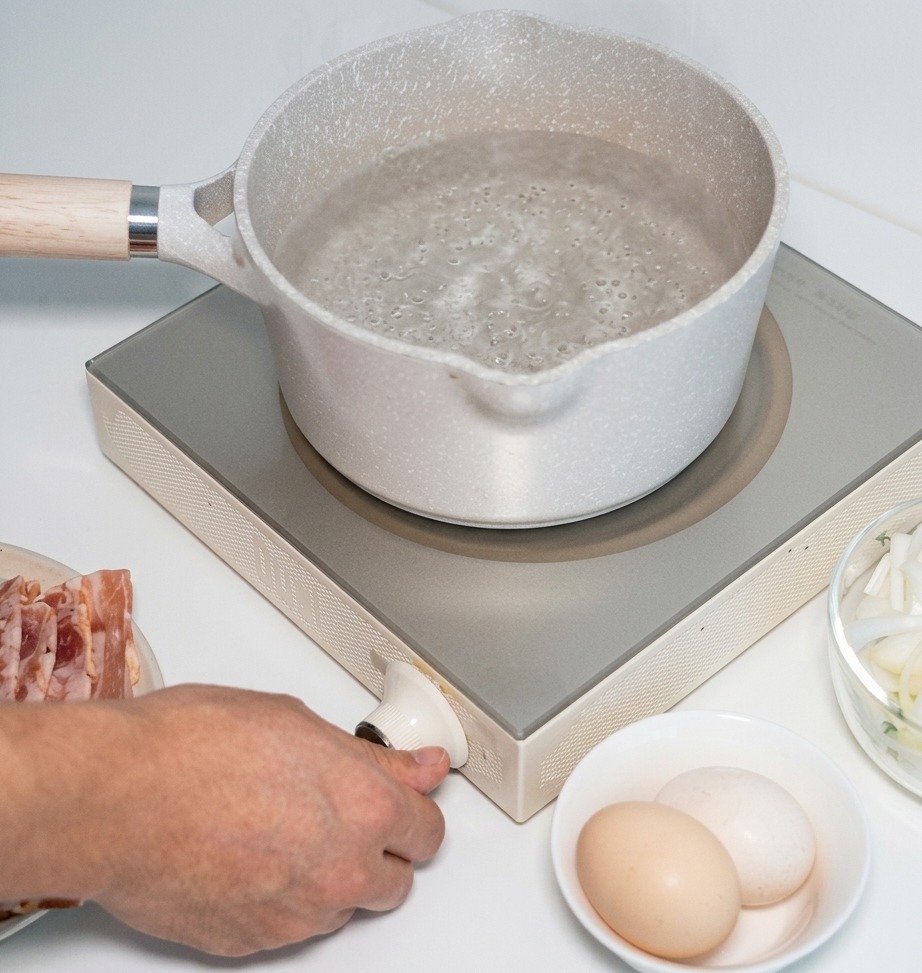Une main règle le bouton dune plaque à induction portable sur laquelle est posée une casserole deau.