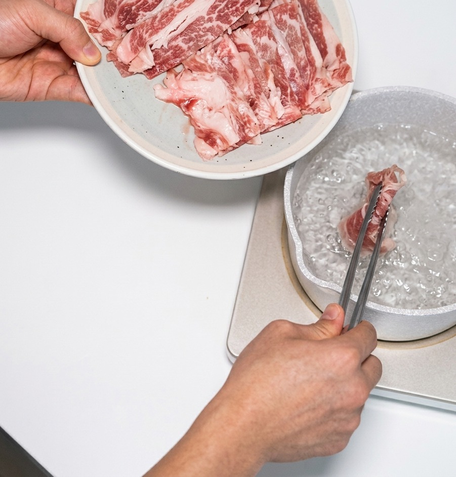 Des fines tranches de bœuf persillé sont plongées dans une casserole deau bouillante à laide dune pince métallique.