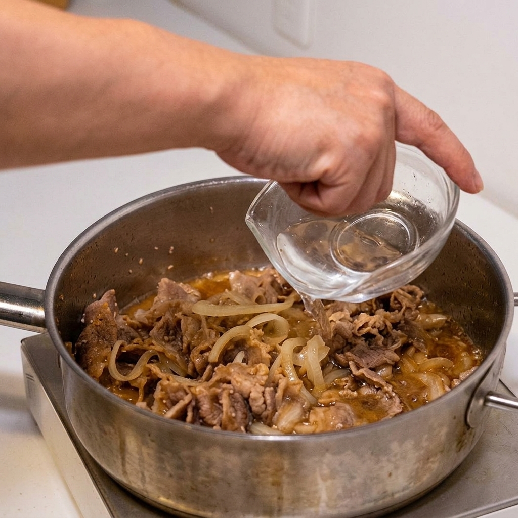 Une main ajoute de leau claire depuis un petit récipient en verre dans la poêle où mijotent le bœuf et la sauce.