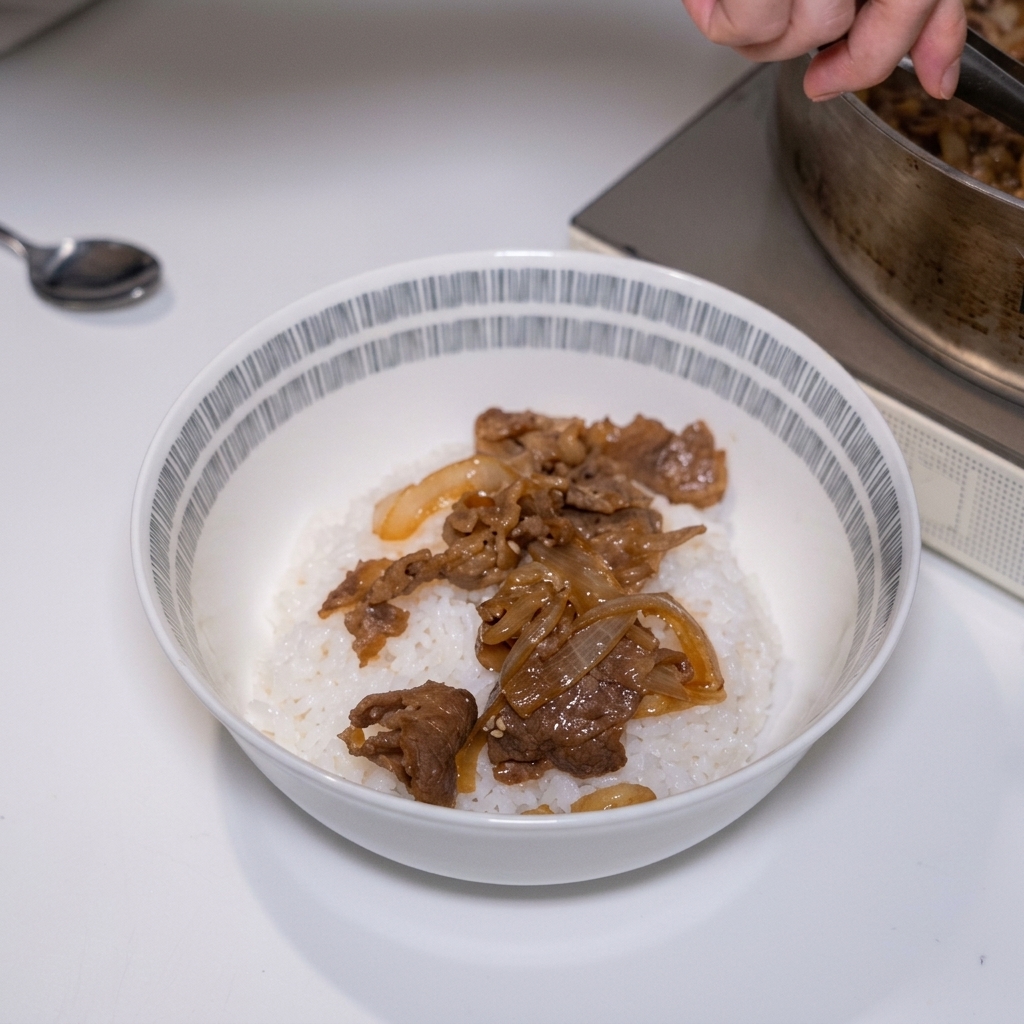 Une pince dépose de généreuses tranches de bœuf mijoté et doignons fondants sur un bol de riz blanc cuit à la vapeur.