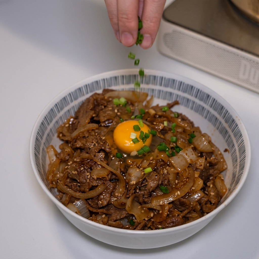 Des doigts parsèment des oignons verts émincés sur un bol de bœuf japonais surmonté dun jaune dœuf.