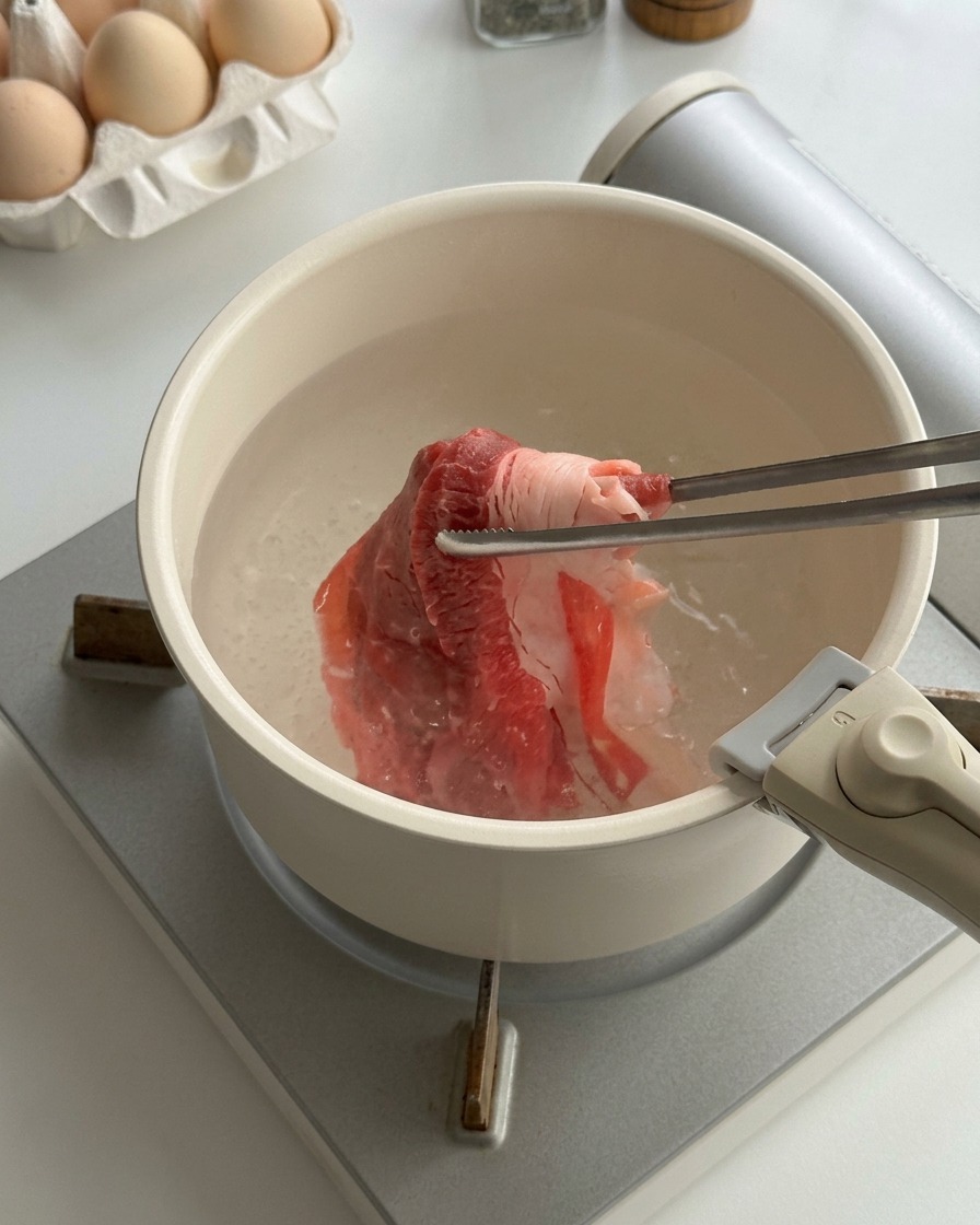 Fines tranches de bœuf cru blanchies dans une casserole deau bouillante avec des baguettes en métal.