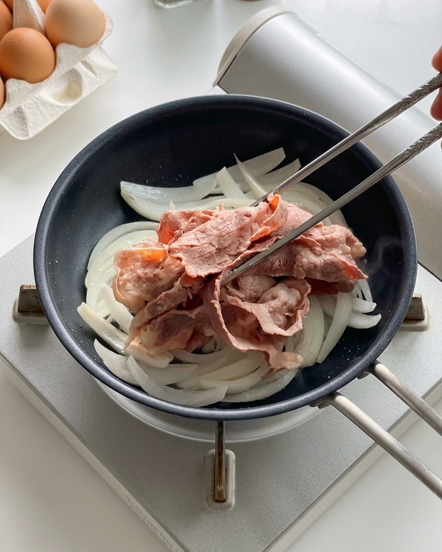 Baguettes en métal déposant les tranches de bœuf blanchies sur les oignons en cours de cuisson dans une poêle.