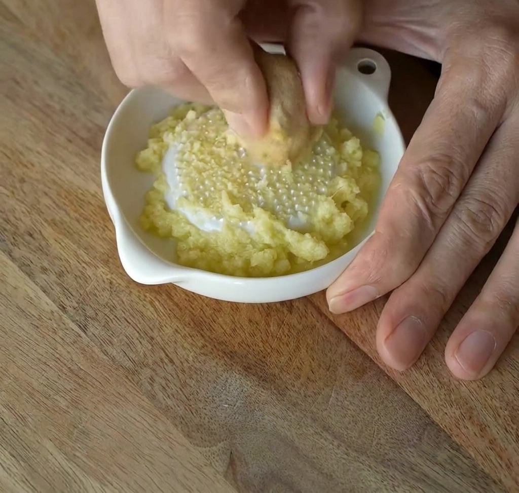 Du gingembre frais frotté contre une râpe en céramique blanche pour obtenir une pâte fine.