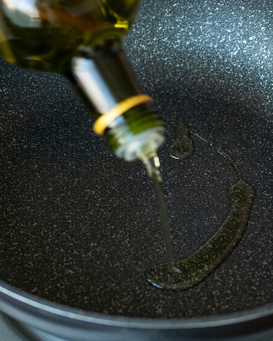 De lhuile davocat claire versée dune bouteille en verre vert sur une poêle antiadhésive sombre et tachetée.