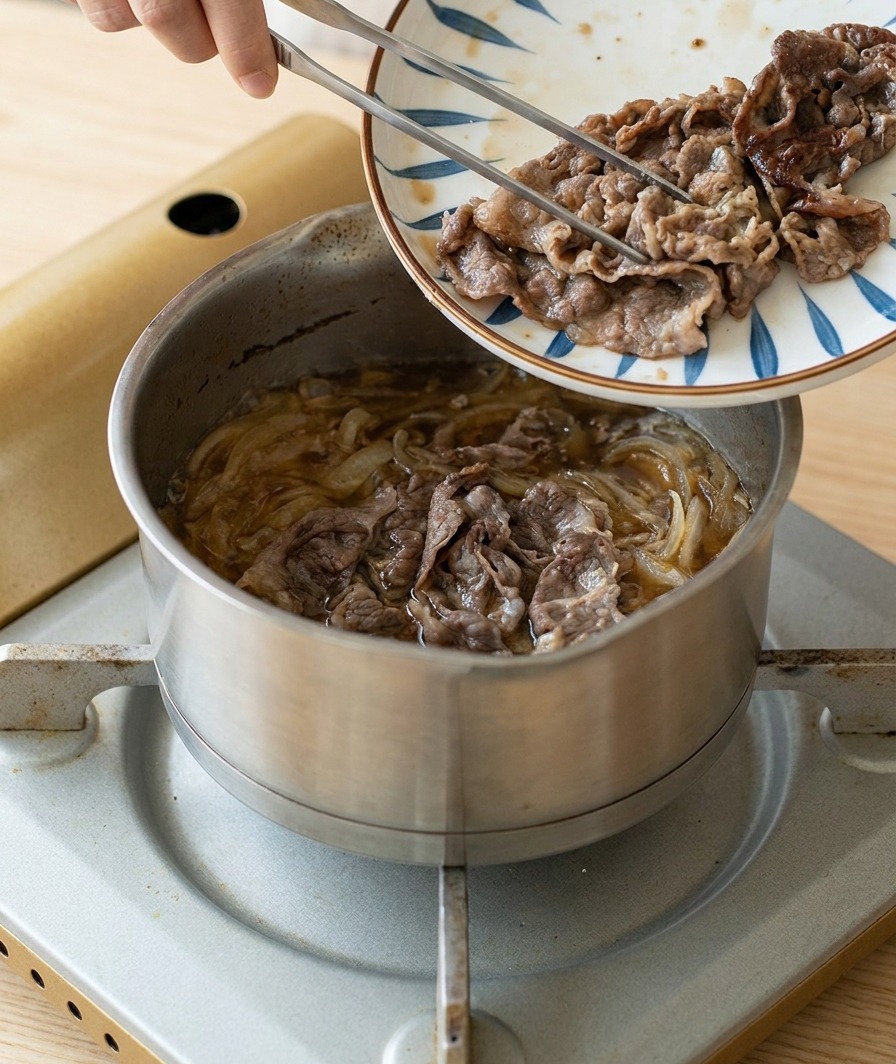Des tranches de bœuf dorées et saisies transférées depuis une assiette décorée vers une casserole doignons et de sauce frémissants.