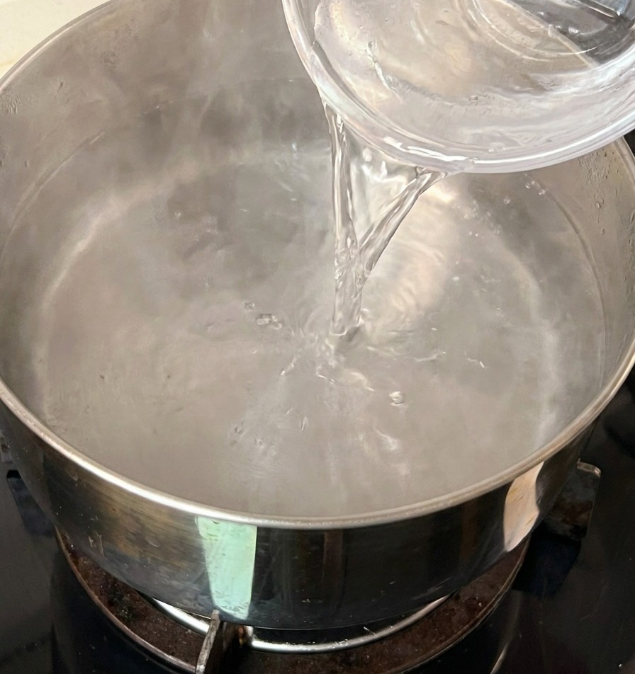 Versement dun petit bol deau froide dans une casserole deau bouillante hors du feu.