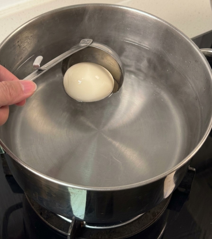 Une louche déposant délicatement un œuf blanc entier dans une casserole deau.