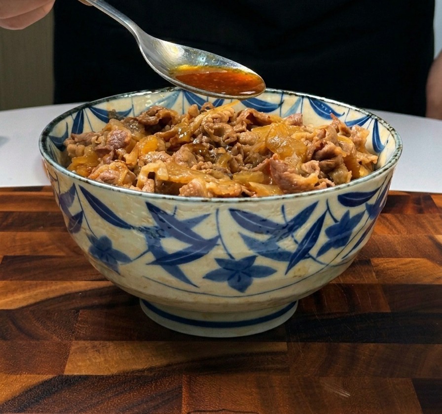 Une cuillère versant une sauce brune savoureuse sur du bœuf émincé et des oignons déposés sur du riz blanc.