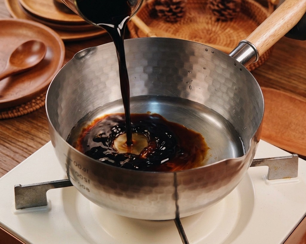De la sauce soja foncée est versée dans une casserole Yukihira contenant déjà de leau et dautres liquides transparents.