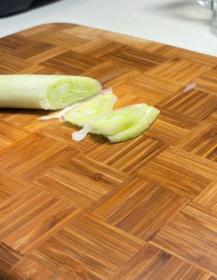 Oignons verts coupés en biseau disposés sur une planche à découper en bois.