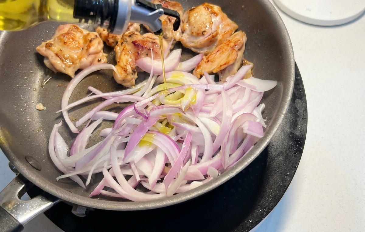 Lamelles doignons rouges ajoutées dans la poêle avec le poulet qui dore, arrosées dun filet dhuile.