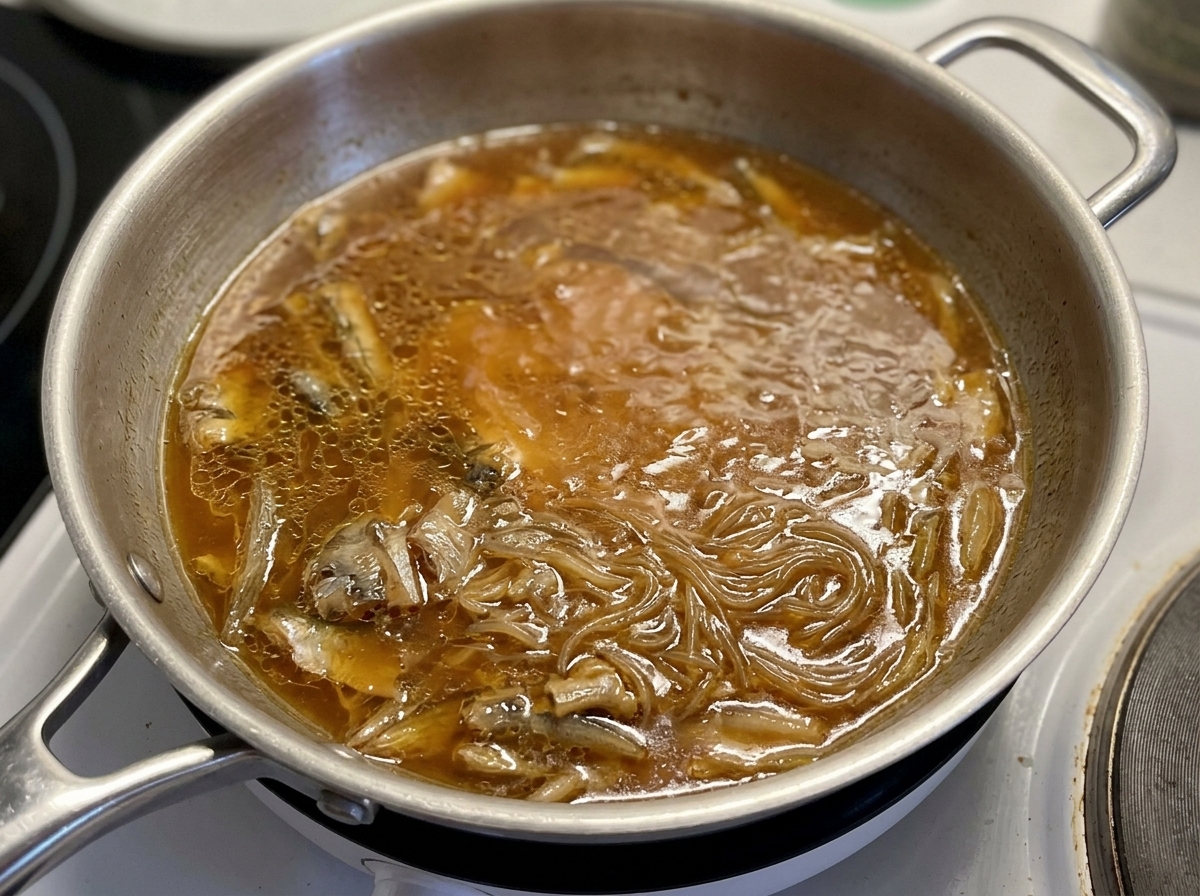 Couvercle en verre posé sur une poêle où le poulet et les oignons mijotent dans une sauce brune.