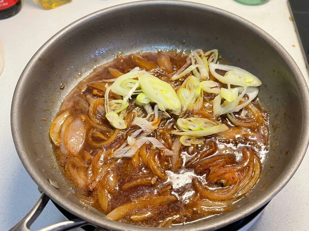 Oignons verts émincés ajoutés dans la poêle contenant la sauce frémissante et les oignons cuits.