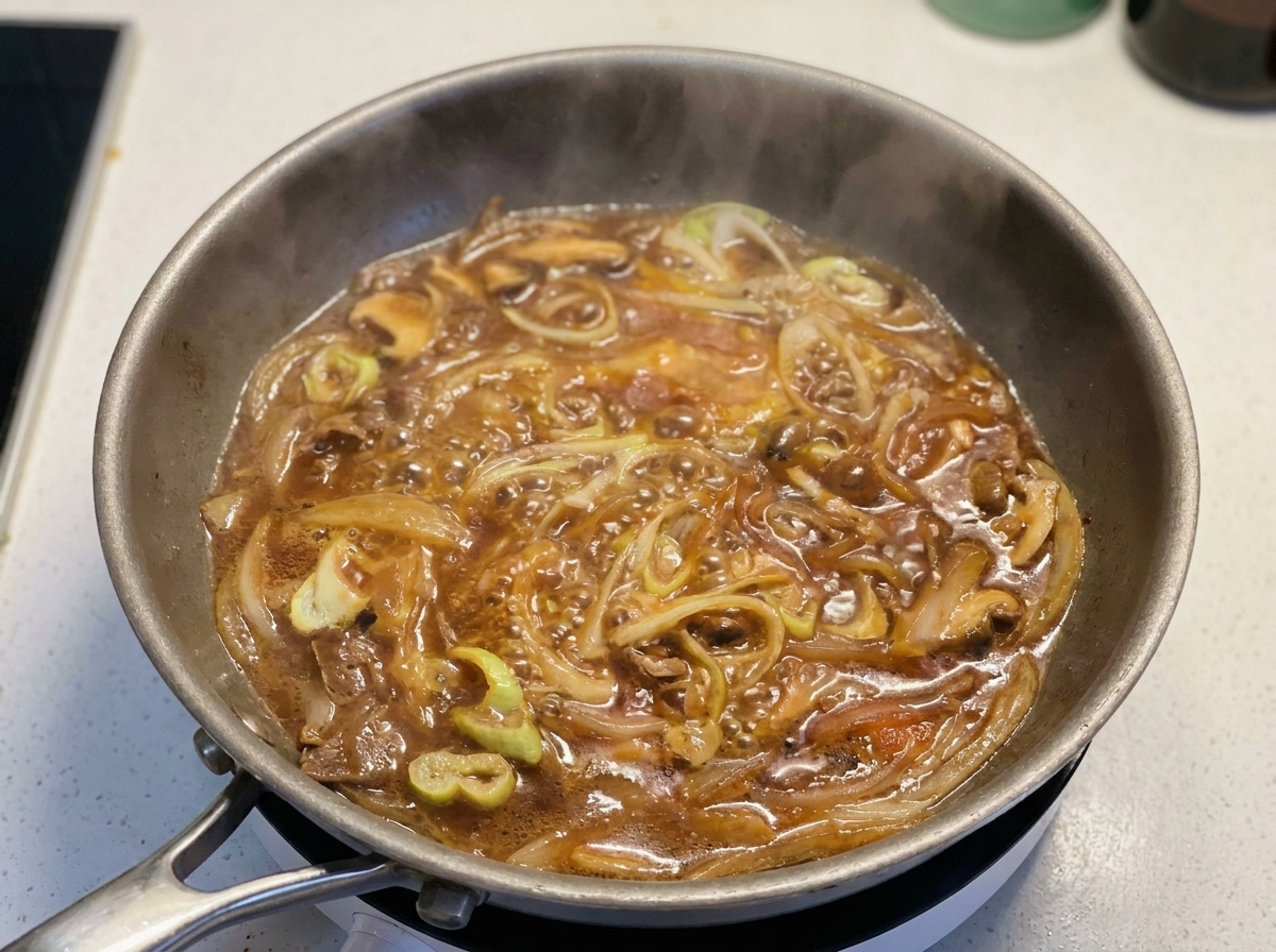 Œufs battus versés en filet dans la poêle avec la sauce frémissante et les oignons.
