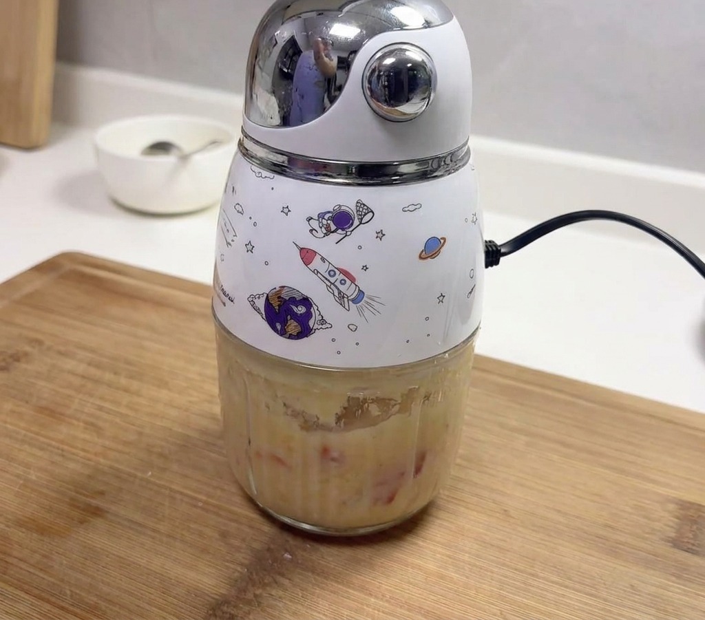 Un petit mixeur électrique décoré contenant une pâte épaisse dail mixé et de piments rouges.