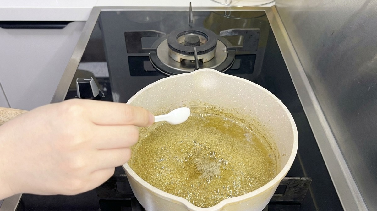 Une personne utilisant une petite cuillère blanche pour ajouter de lassaisonnement à un liquide bouillant légèrement verdâtre dans une casserole.