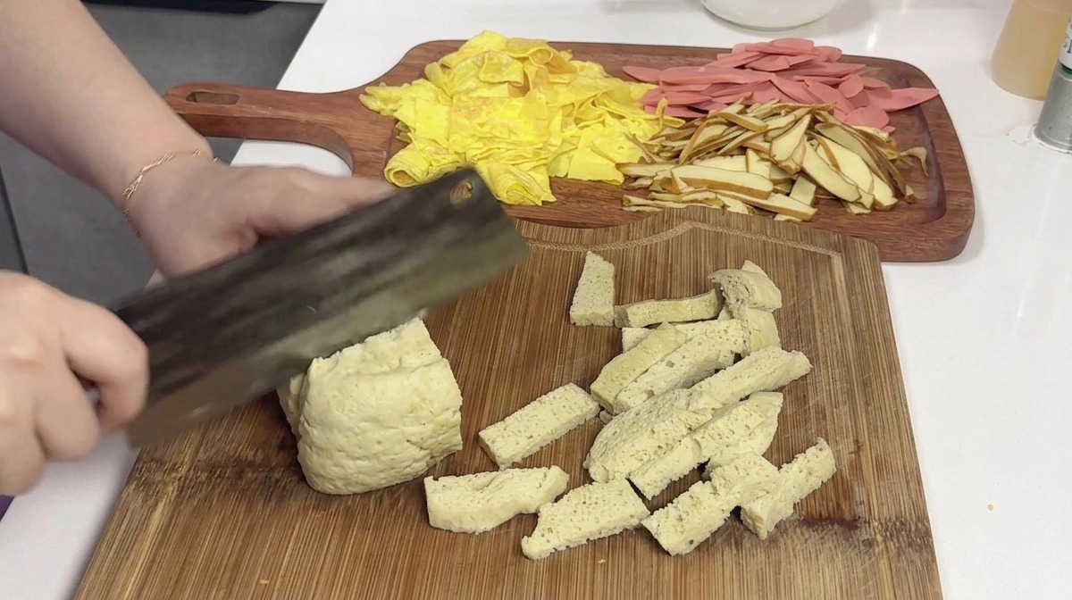 Un grand bloc de gluten à la vapeur clair et spongieux coupé en portions rectangulaires sur une planche en bois à laide dun couperet.