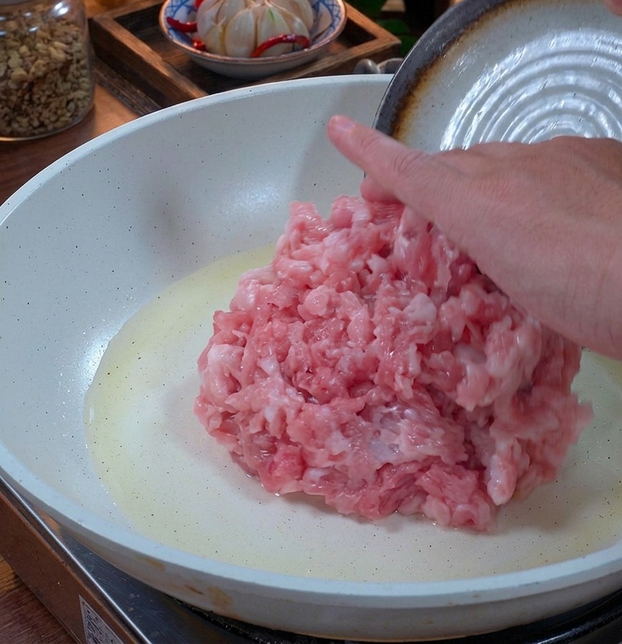 Porc haché frais et rose déposé dans une poêle en céramique blanche avec un léger filet dhuile.
