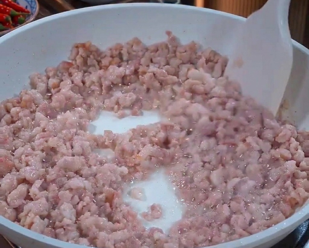 Porc haché remué dans une poêle blanche avec une spatule blanche, passant de la couleur rose au gris clair.
