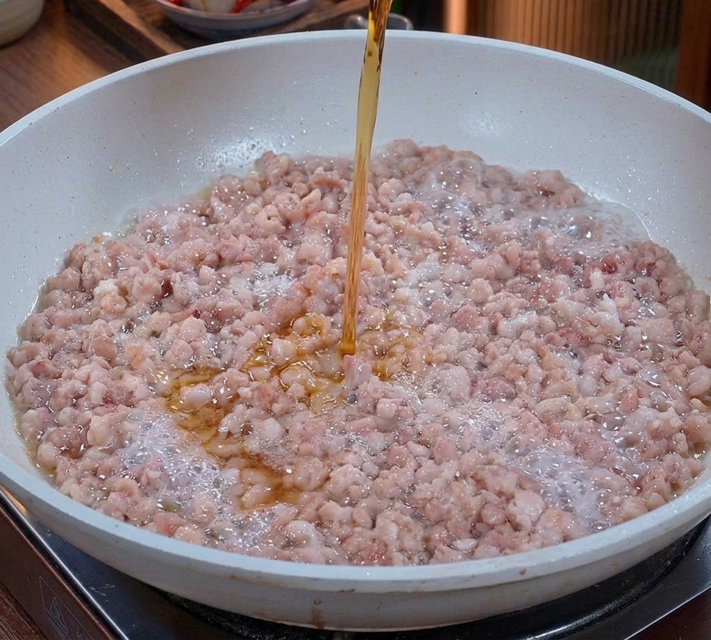 Un liquide ambré clair versé dun verre sur du porc haché en train de sauter dans une poêle.