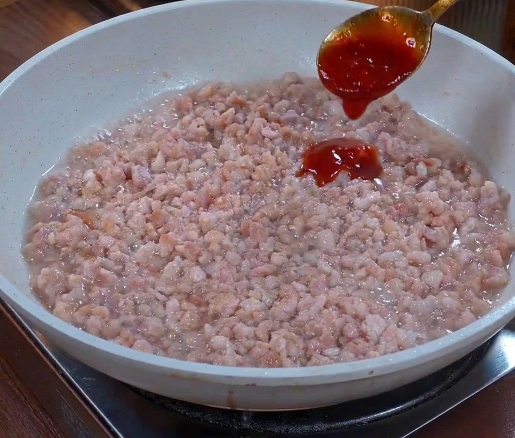 Une cuillère en métal versant une sauce marron foncé et épaisse sur un lit de viande hachée sautée dans une poêle.