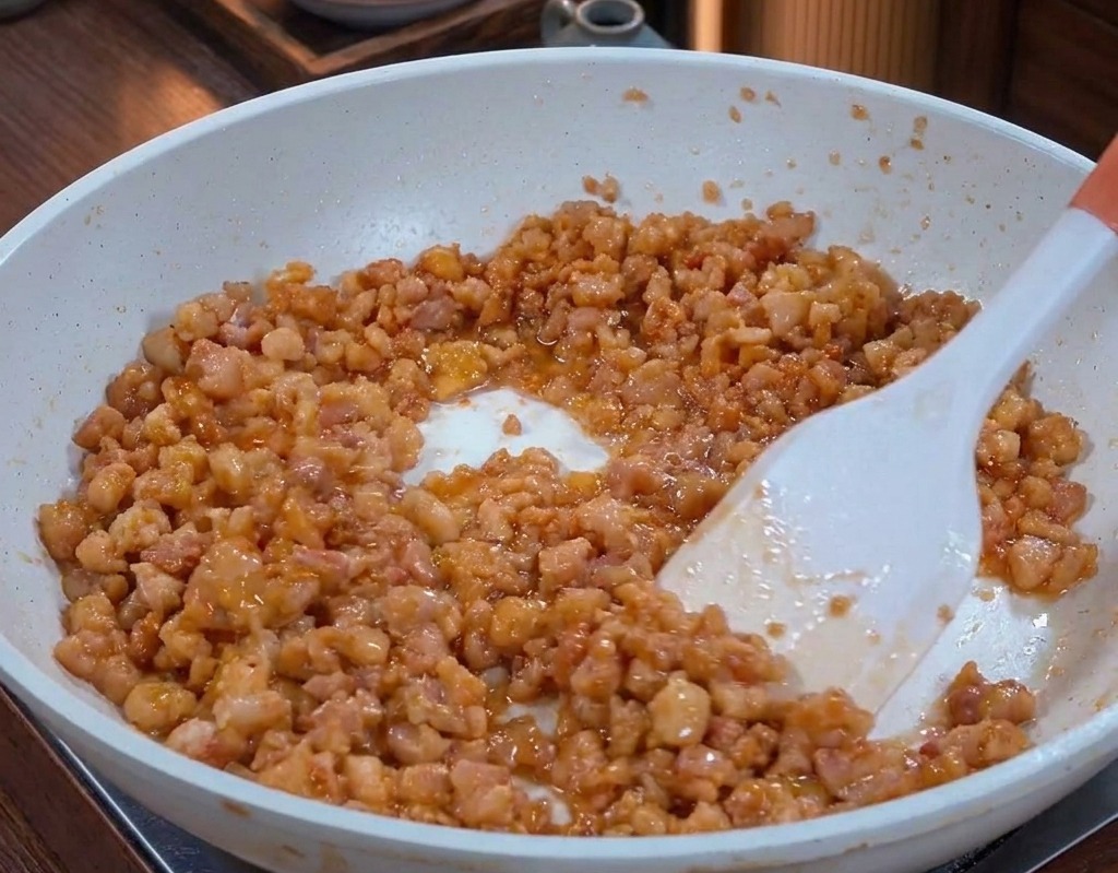 Porc haché cuit dans une poêle, brillant de graisse fondue et visiblement caramélisé et doré.