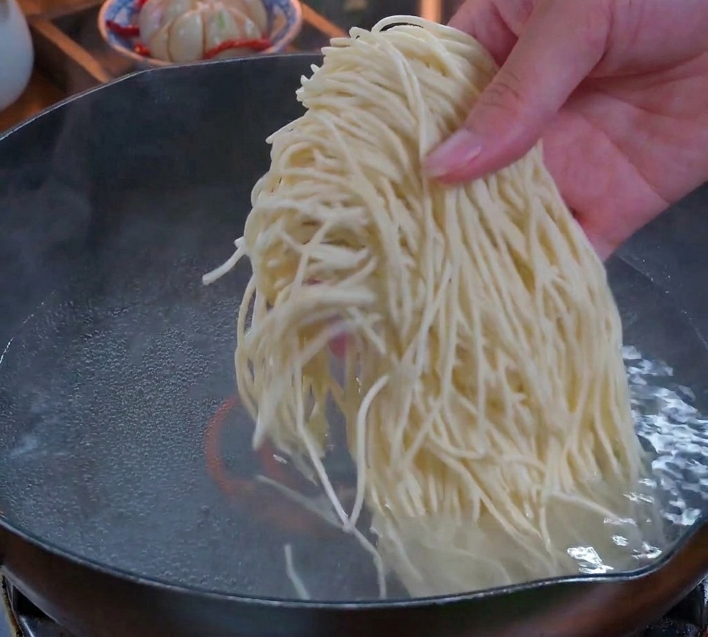 Une main plongeant un paquet de nouilles fraîches et fines dans une casserole deau bouillante.
