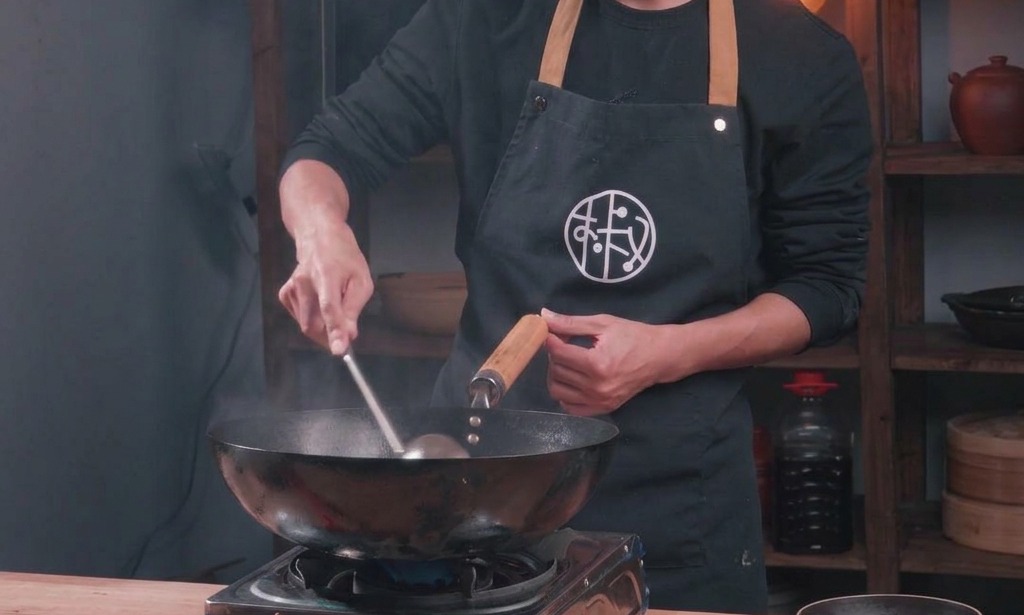 Un cuisinier fait sauter du porc haché dans un wok traditionnel en y ajoutant un assaisonnement liquide.