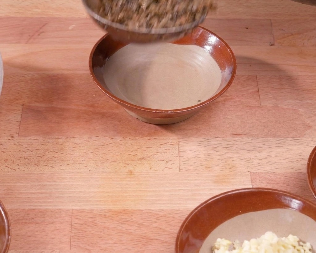 Une louche transférant le mélange de porc et de légumes cuits dans un bol en céramique brune sur une table en bois.