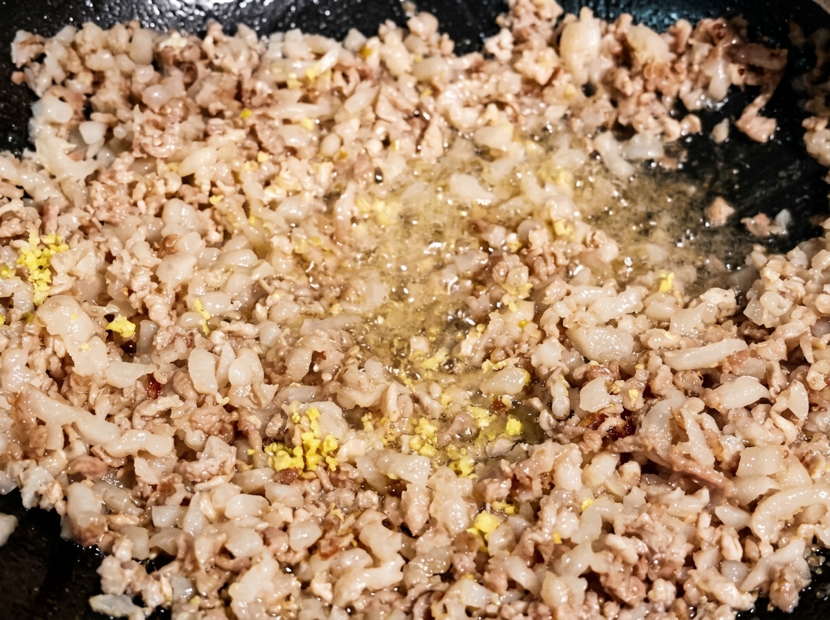 Morceaux de gingembre et dail hachés sautés avec la viande hachée dorée dans un wok sombre.