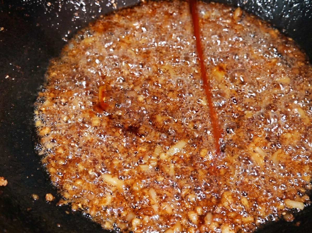 Un filet dassaisonnement sombre ajouté au porc haché dans un wok, fonçant la couleur de lensemble.