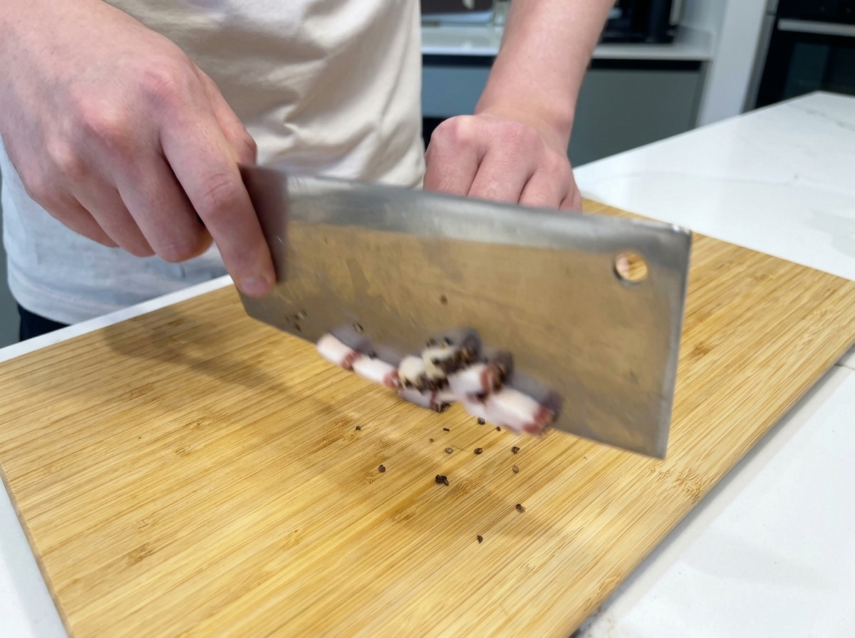Un chef utilisant un grand couteau pour couper des bandes de guanciale en petits cubes sur une planche en bambou.