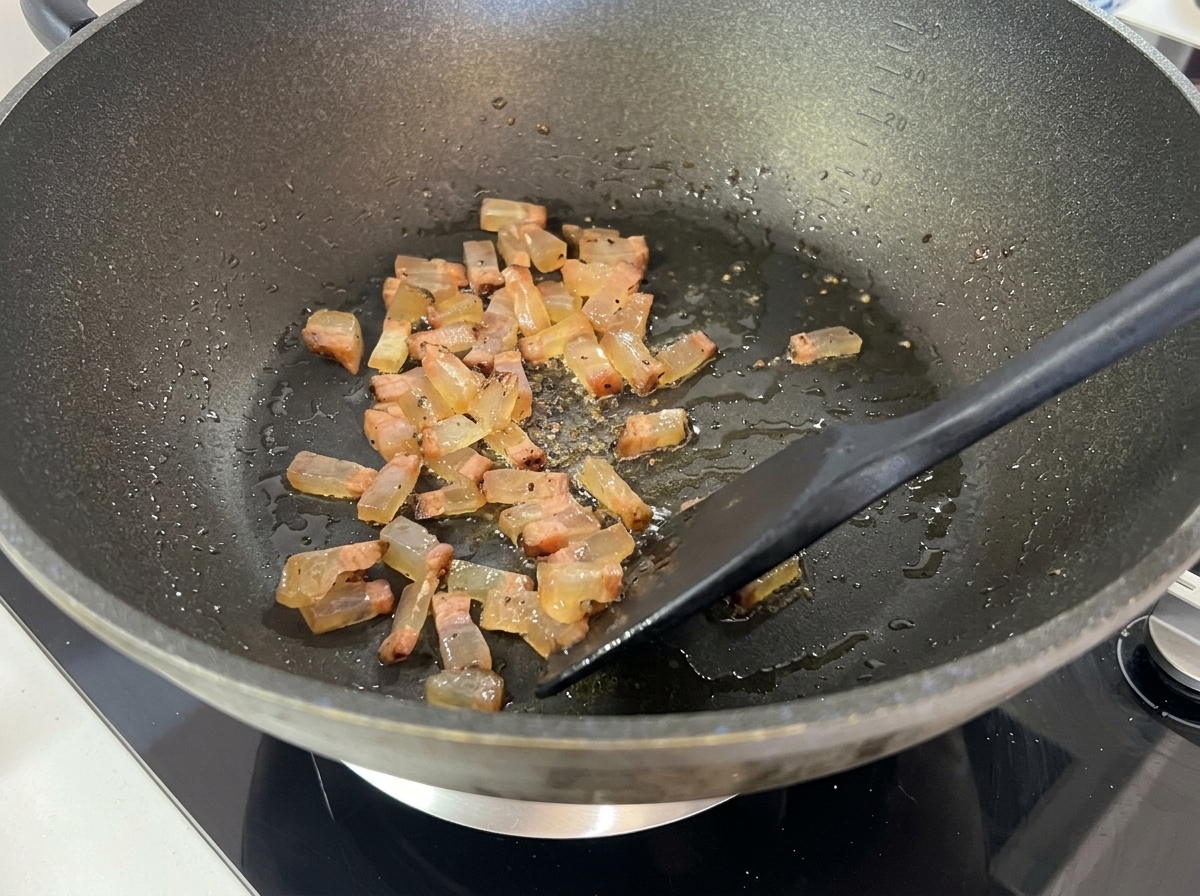 Dés de guanciale brunissant et devenant translucides dans un wok, libérant activement du gras liquide.