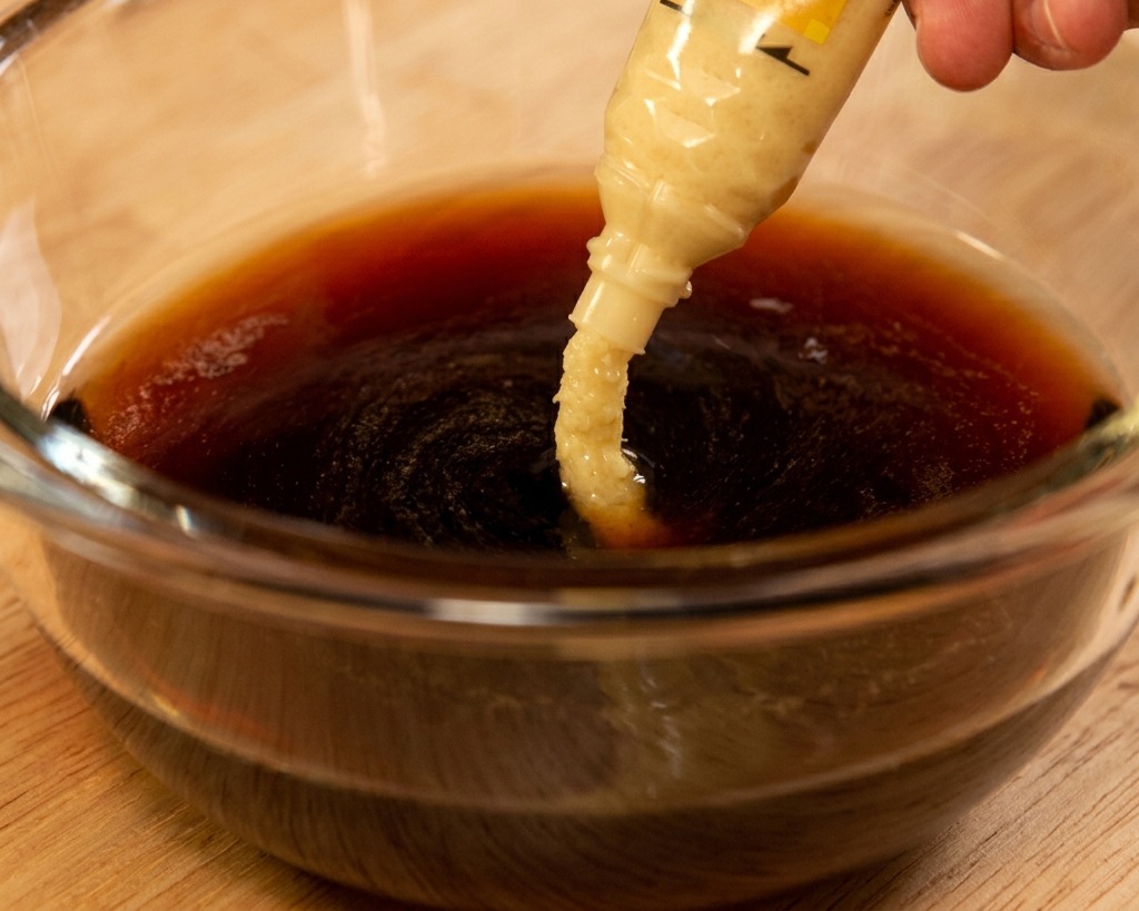 De la pâte de gingembre frais pressée depuis un tube dans une sauce sombre à base de soja.