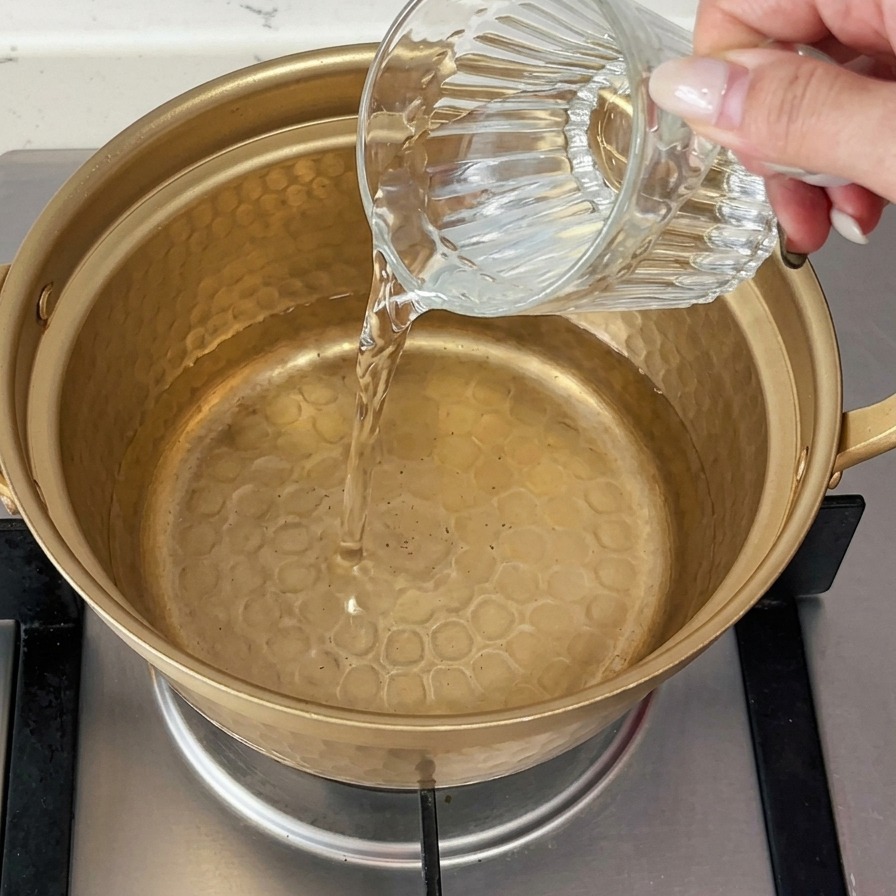 De leau froide est versée dun verre dans une petite casserole en métal de couleur dorée posée sur une cuisinière à gaz.