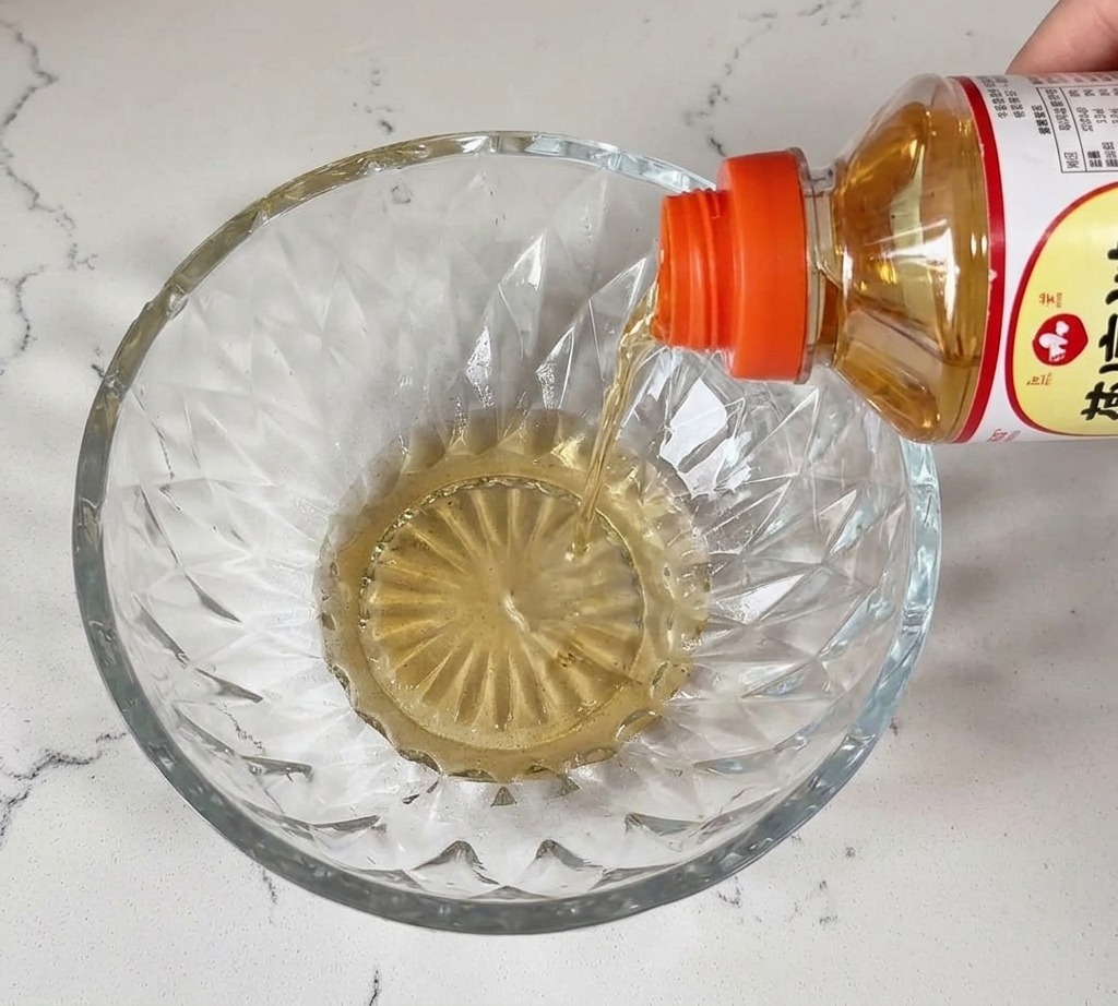 Du mirin liquide et transparent est versé dune bouteille dans un bol en cristal sur un plan de travail blanc.