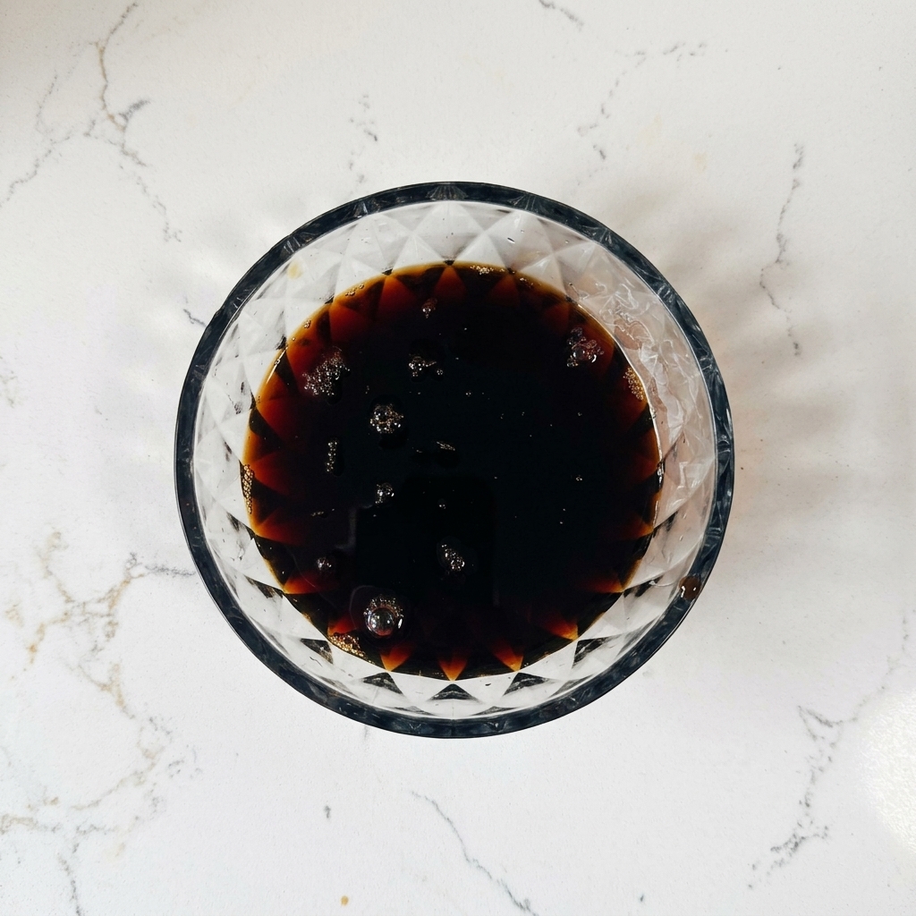 Une vue plongeante dun bol en verre contenant une sauce liquide marron foncé avec de petites bulles dair à la surface.