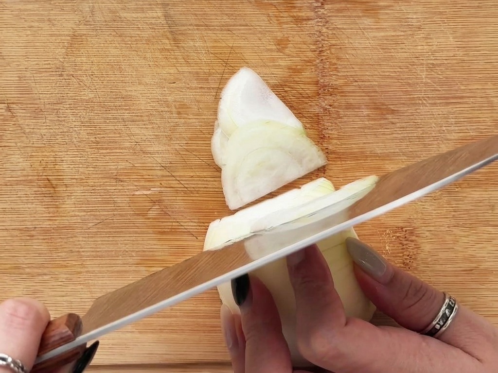 Des mains coupant un oignon blanc en fines demi-lunes sur une planche à découper en bois.