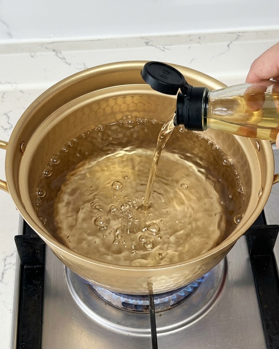 Verser du vin de cuisine transparent depuis une bouteille en verre dans une casserole dorée remplie deau bouillante.