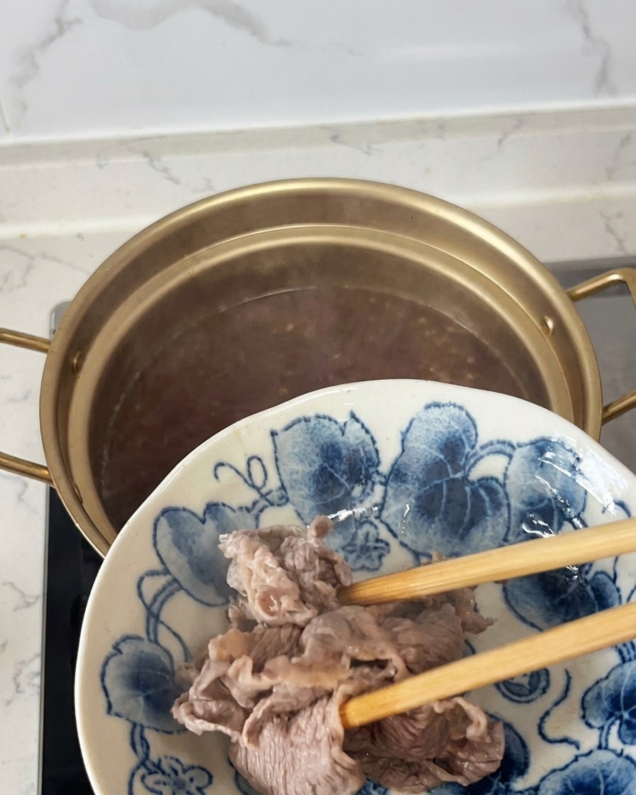 Soulever des tranches de bœuf partiellement cuites et opaques hors dune casserole avec des baguettes et les transférer sur une assiette à motifs bleus et blancs.