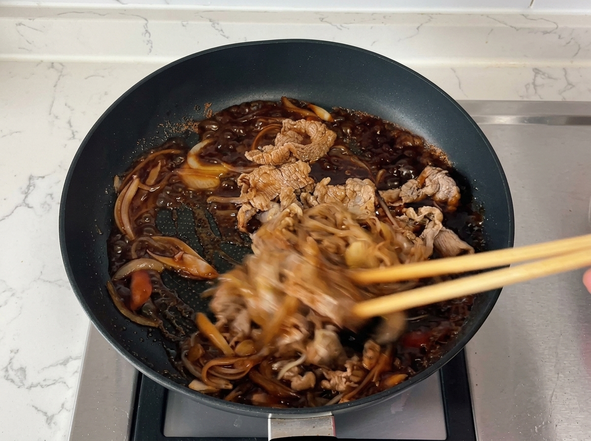 Des baguettes remuant rapidement du bœuf et des oignons dans une sauce foncée qui bouillonne et sépaissit.
