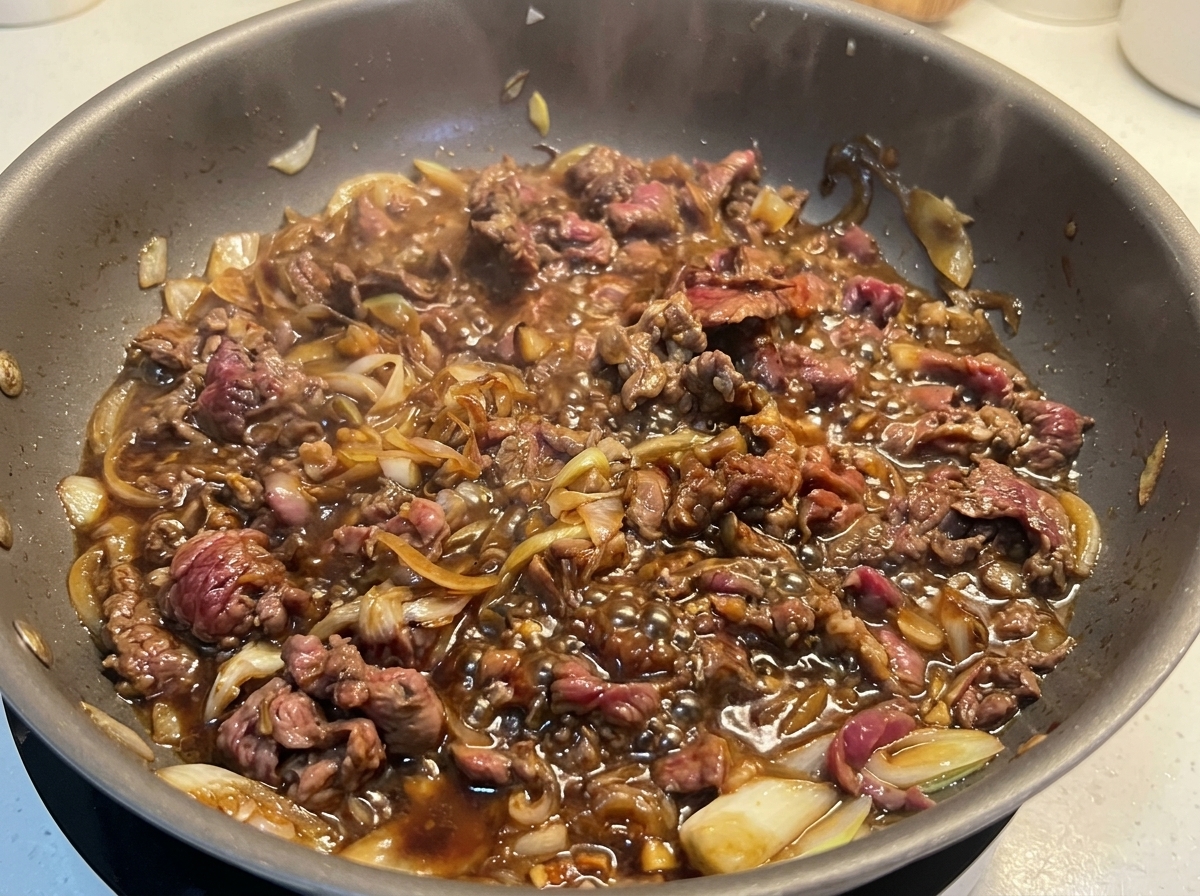 Fines tranches de bœuf bien dorées mijotant activement dans une sauce sombre et bouillonnante avec des oignons.