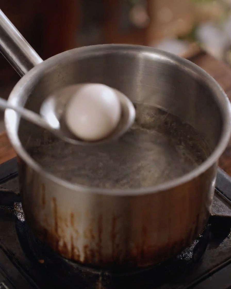 Un œuf blanc entier descendu délicatement dans une casserole deau bouillante à laide dune louche métallique.