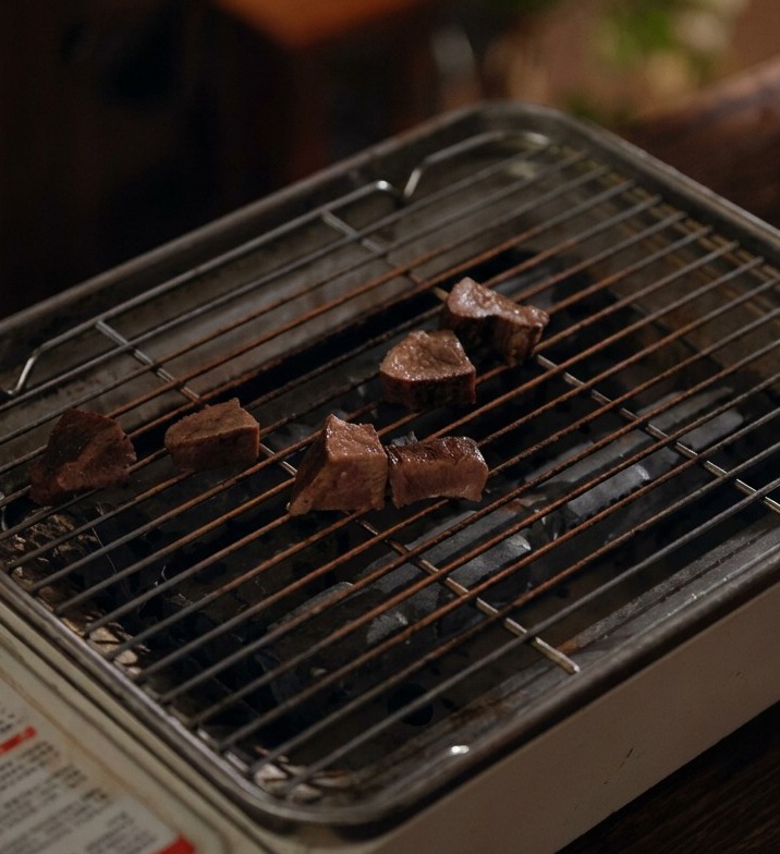 Tranches de langue de bœuf mijotée disposées sur une petite grille métallique portable au-dessus du charbon de bois.