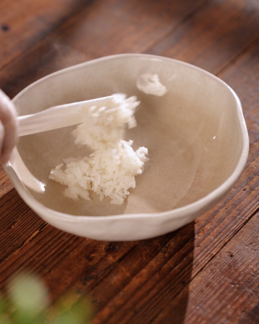 Une spatule à riz transférant du riz blanc fumant et bien détaché dans un bol en céramique beige clair.