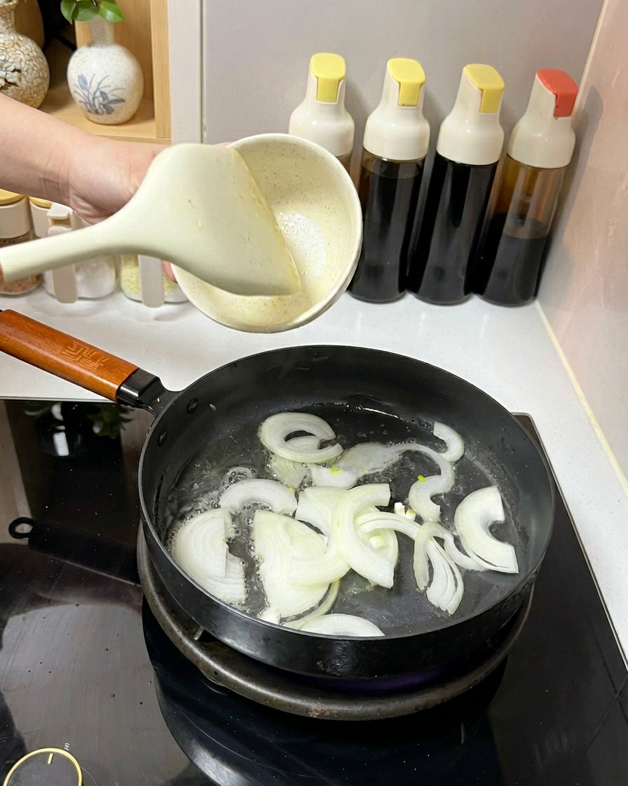 Tranches doignon blanc sautées dans une poêle avec de lhuile à laide dune spatule blanche.