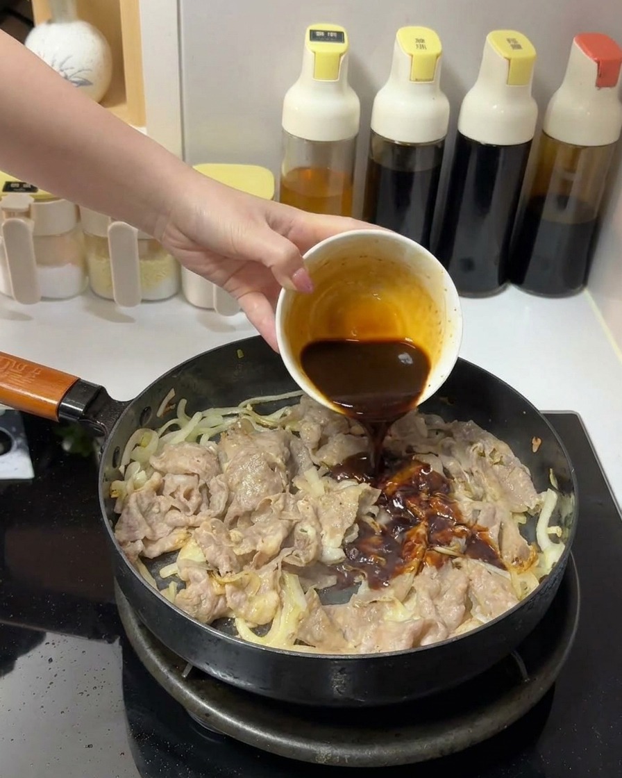 Une sauce brune et épaisse versée depuis un petit bol blanc sur le bœuf et les oignons dans une poêle.
