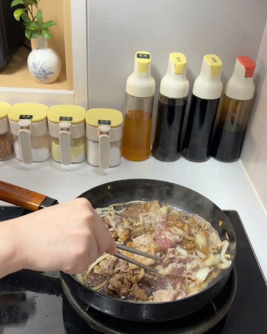 Bœuf et oignons mélangés avec une sauce sombre et brillante dans une poêle à laide de baguettes en métal.